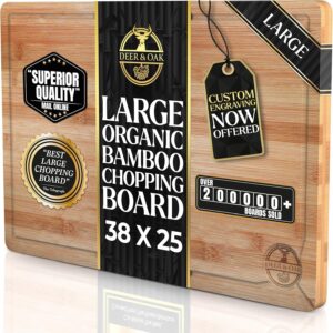 A professional-grade rectangular bamboo cutting board by Deer & Oak, shown in its retail packaging. The board features a light-toned, natural wood grain with a built-in juice groove around the perimeter and a small brand logo etched in the bottom right corner.